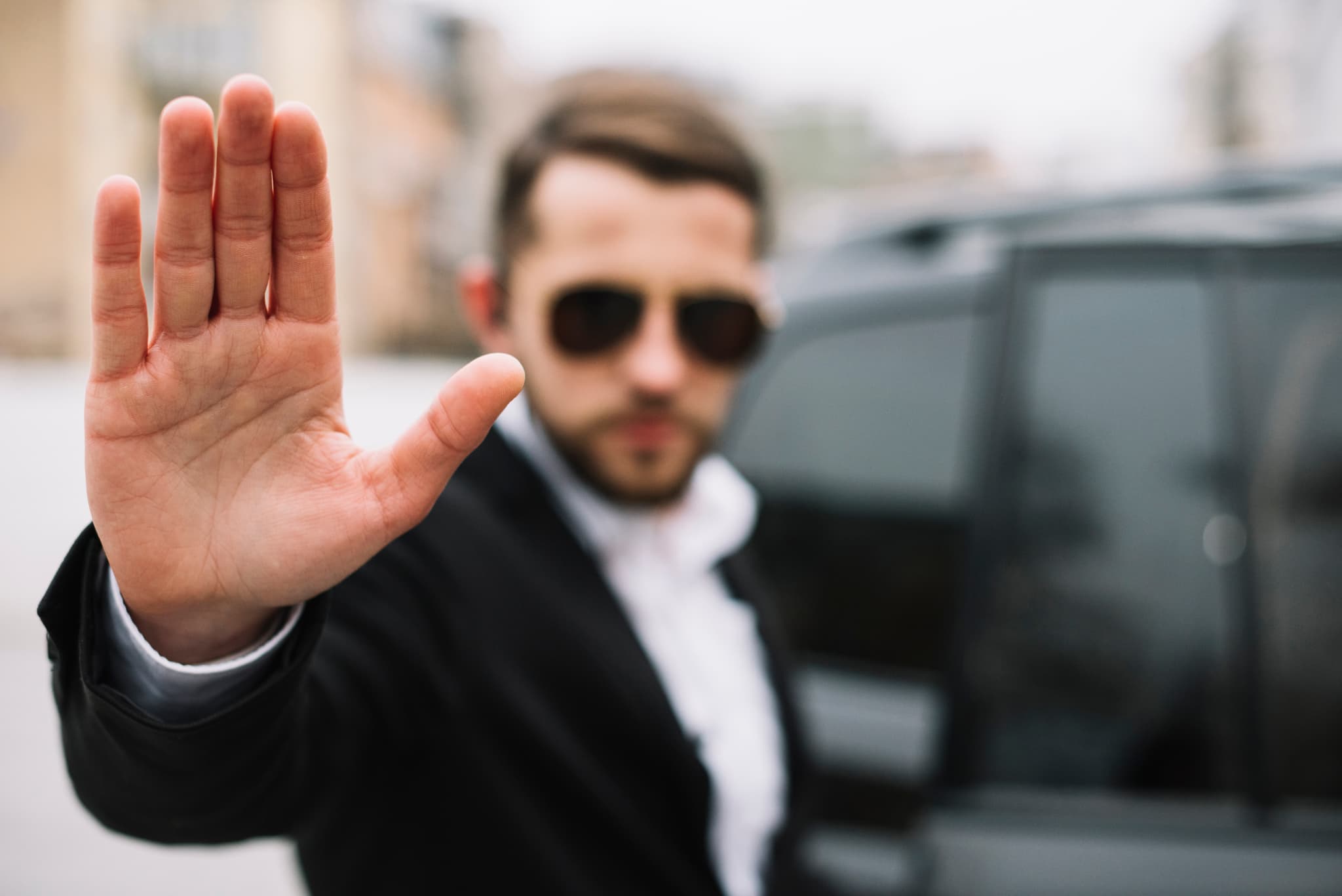 a bodyguard stopping the advance towards a car with an open palm in front